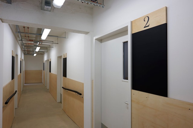 A plywood lining connects each of the studios of a central corridor