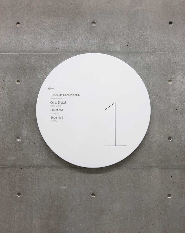 Wayfinding signage appears on shiny metal discs that stand in contrast to the building's walls.